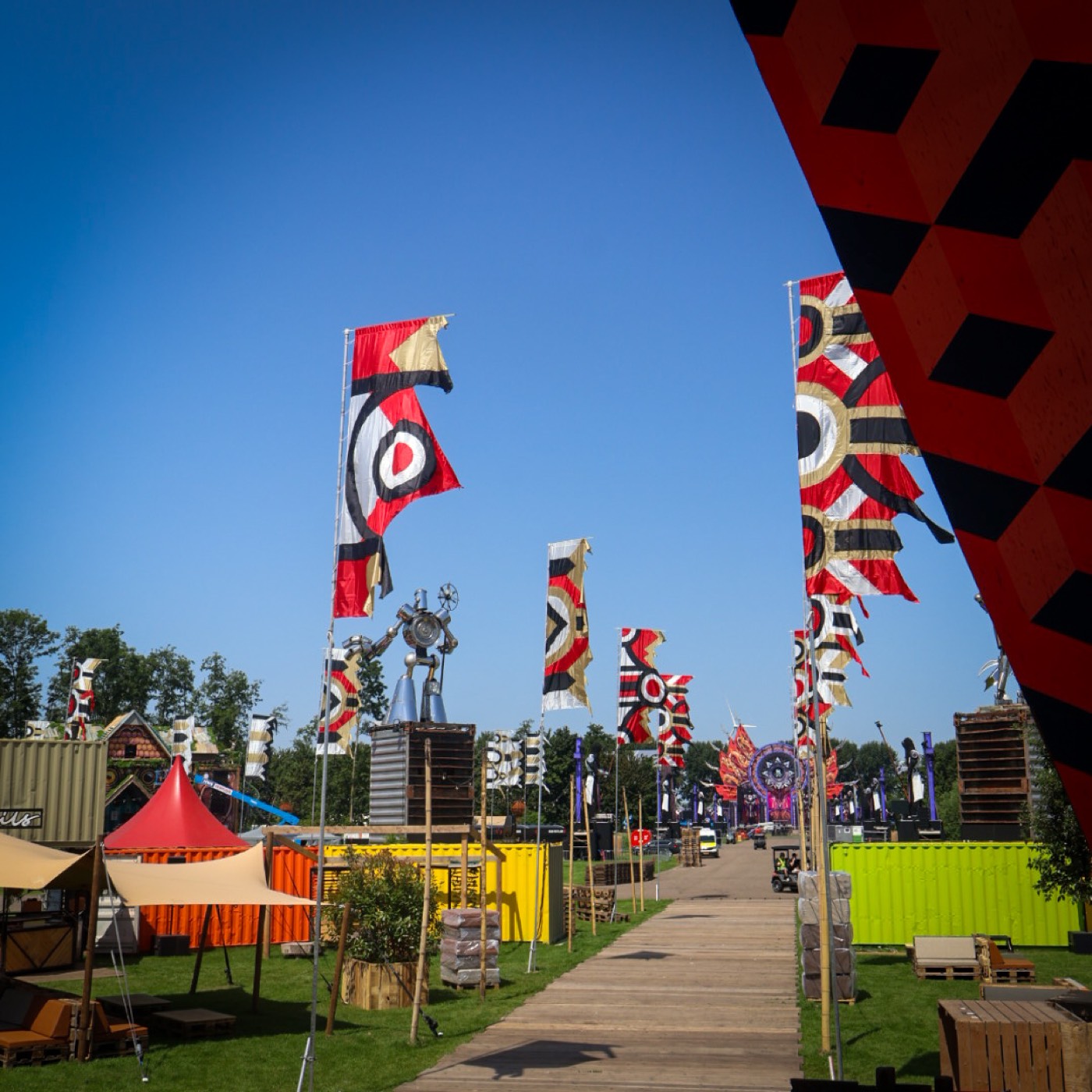 Festivalterrein in opbouw met sierlijke vlaggen, gekleurde containers en een robotsculptuur