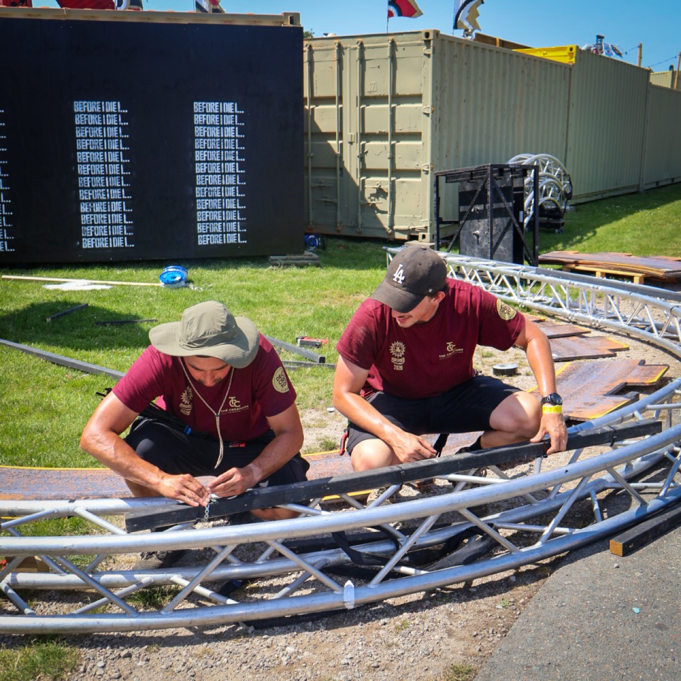 Twee decorbouwers monteren samen een gebogen trussring op een festivalterrein