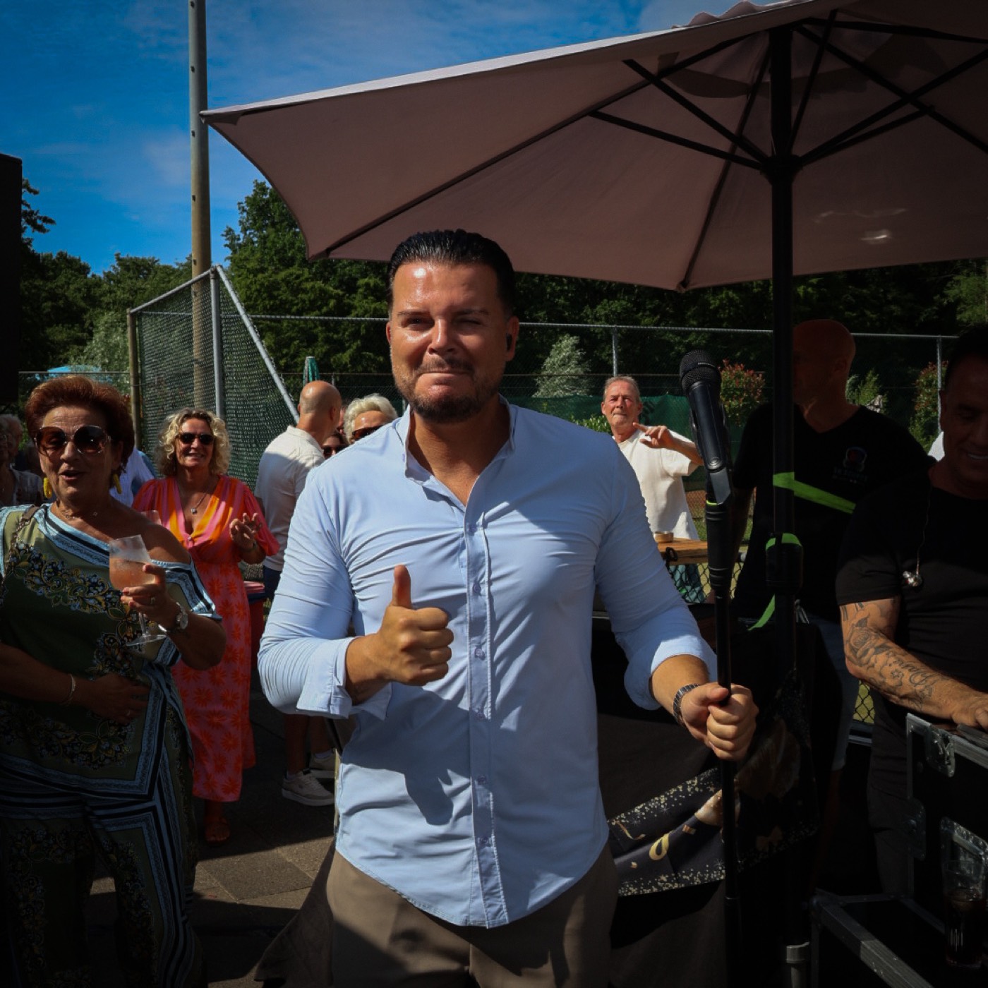 Mike Peterson geeft lachend een duim omhoog aan de camera tussen feestgangers