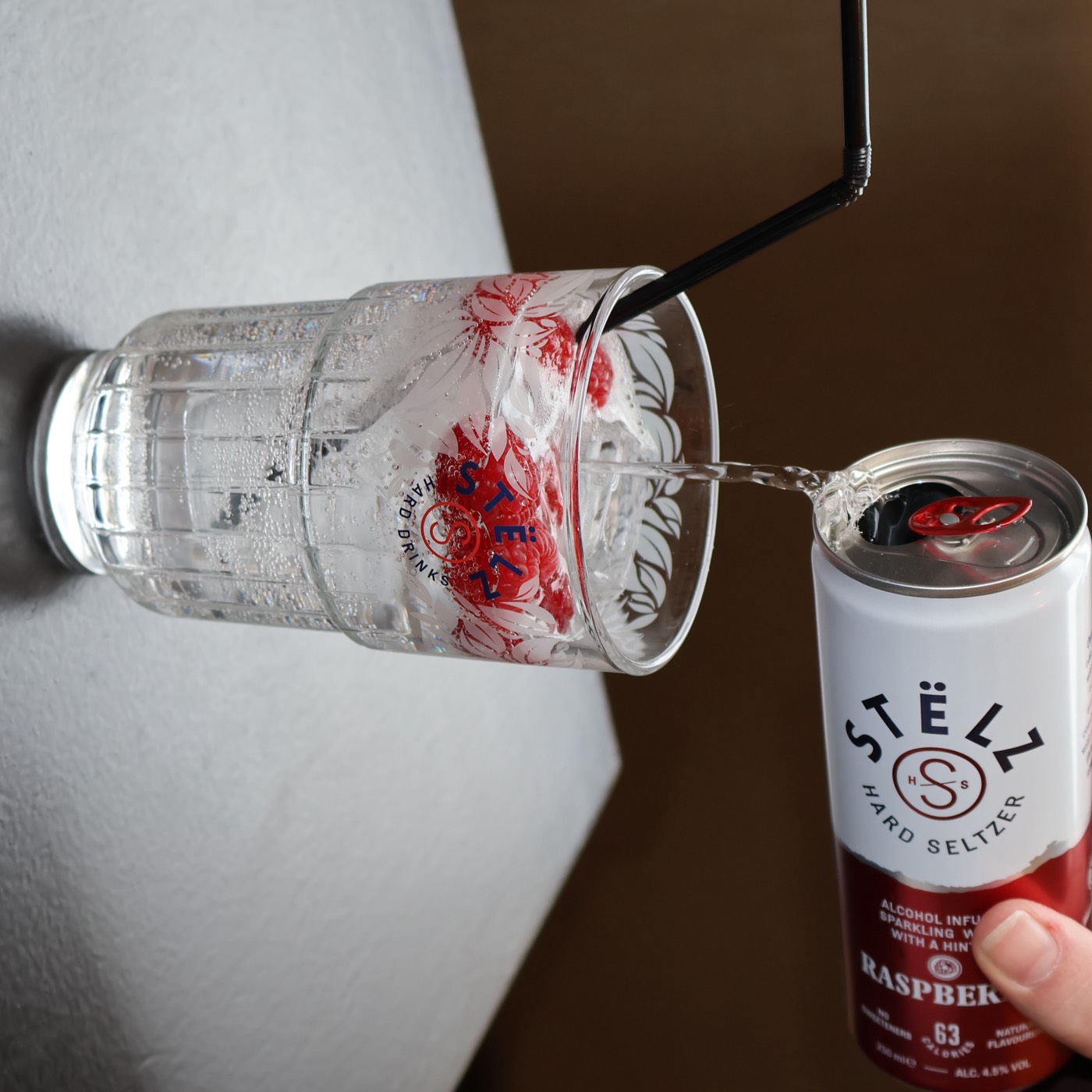 STËLZ raspberry hard seltzer wordt uit het blikje in een glas met verse frambozen geschonken