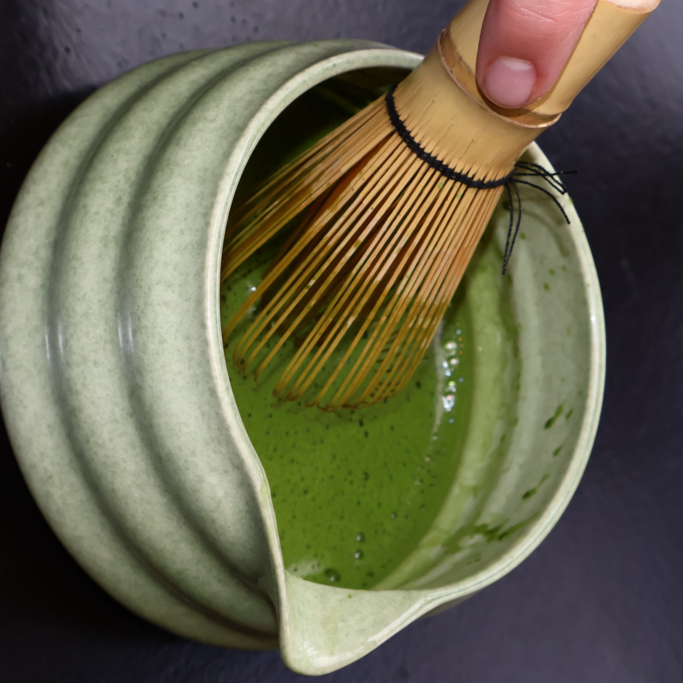 Felgroene matcha wordt geklopt met een bamboe garde in een keramieken kom