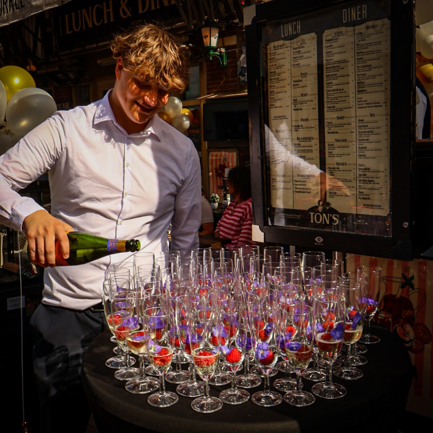 Ober schenkt champagne in glazen met aardbeien en eetbare bloemen