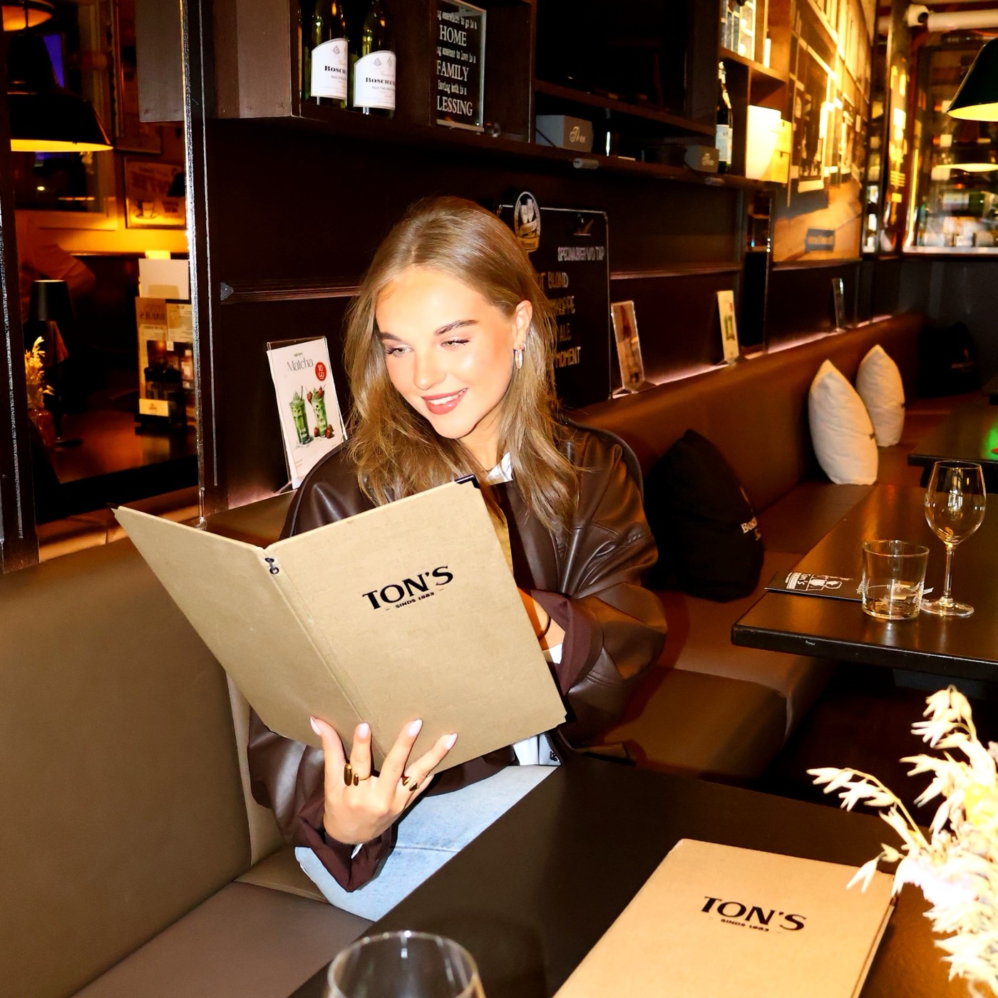 Lachende vrouw leest de opengeslagen Ton's-menukaart in een booth van het café