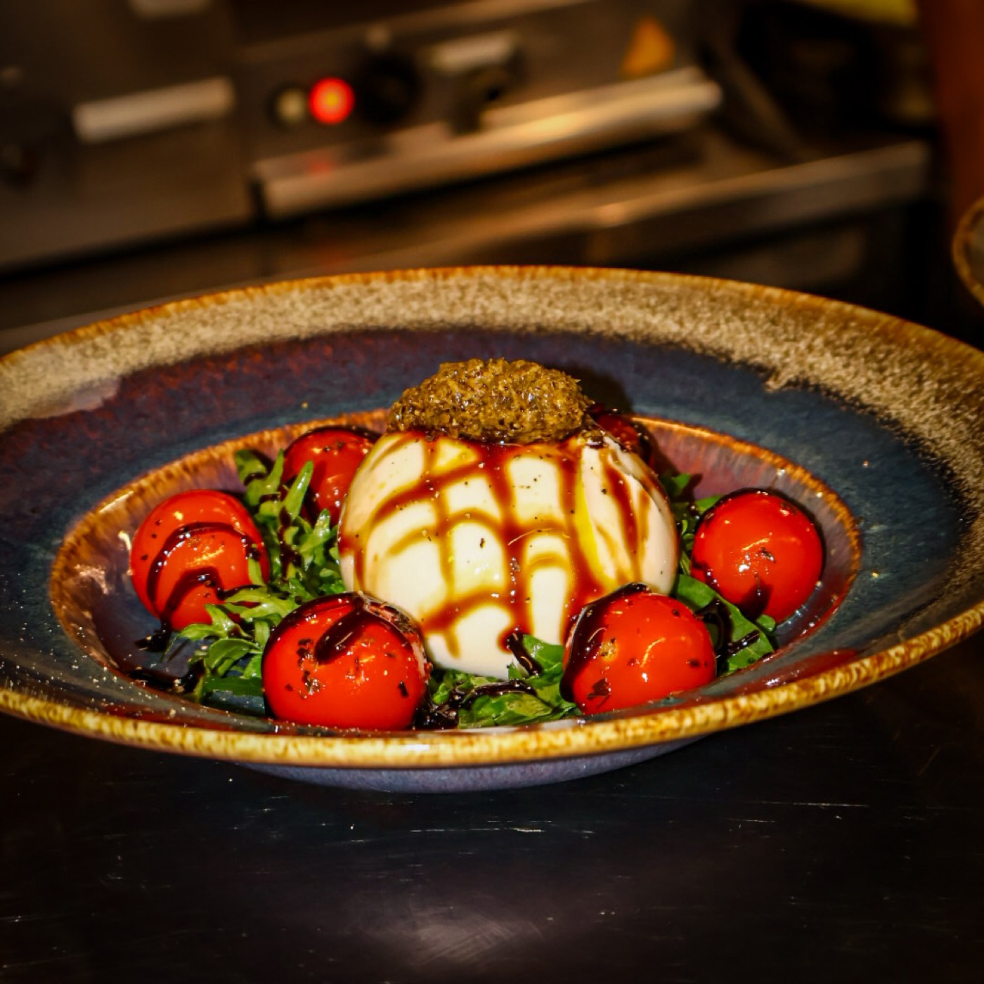 Burrata met pesto, gegrilde cherrytomaten en balsamico in een blauwe keramische schaal