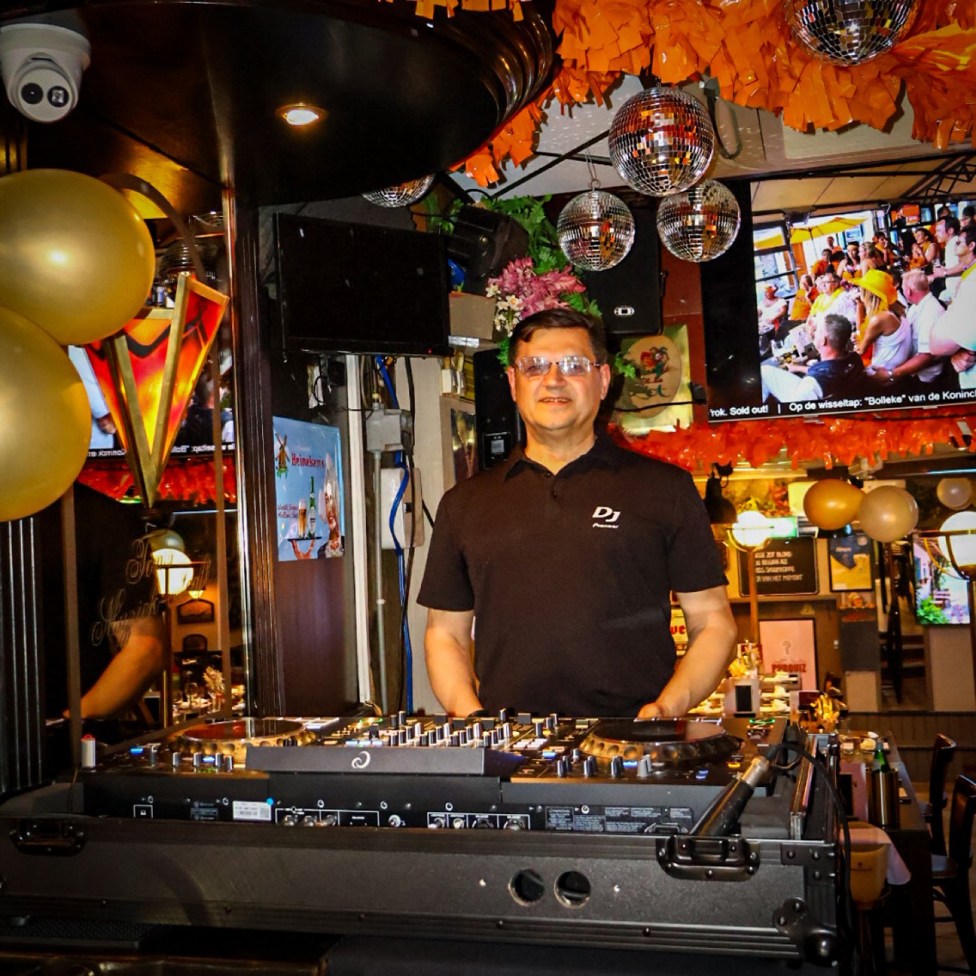 DJ achter de draaitafels onder discoballen in Ton's Muziek Café